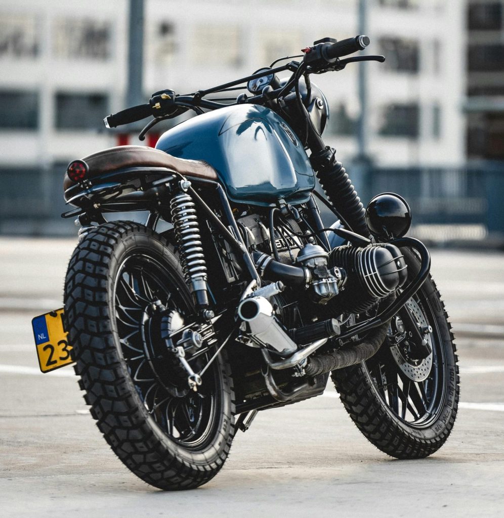 A sleek cafe racer motorcycle parked on asphalt with modern architecture in the background.