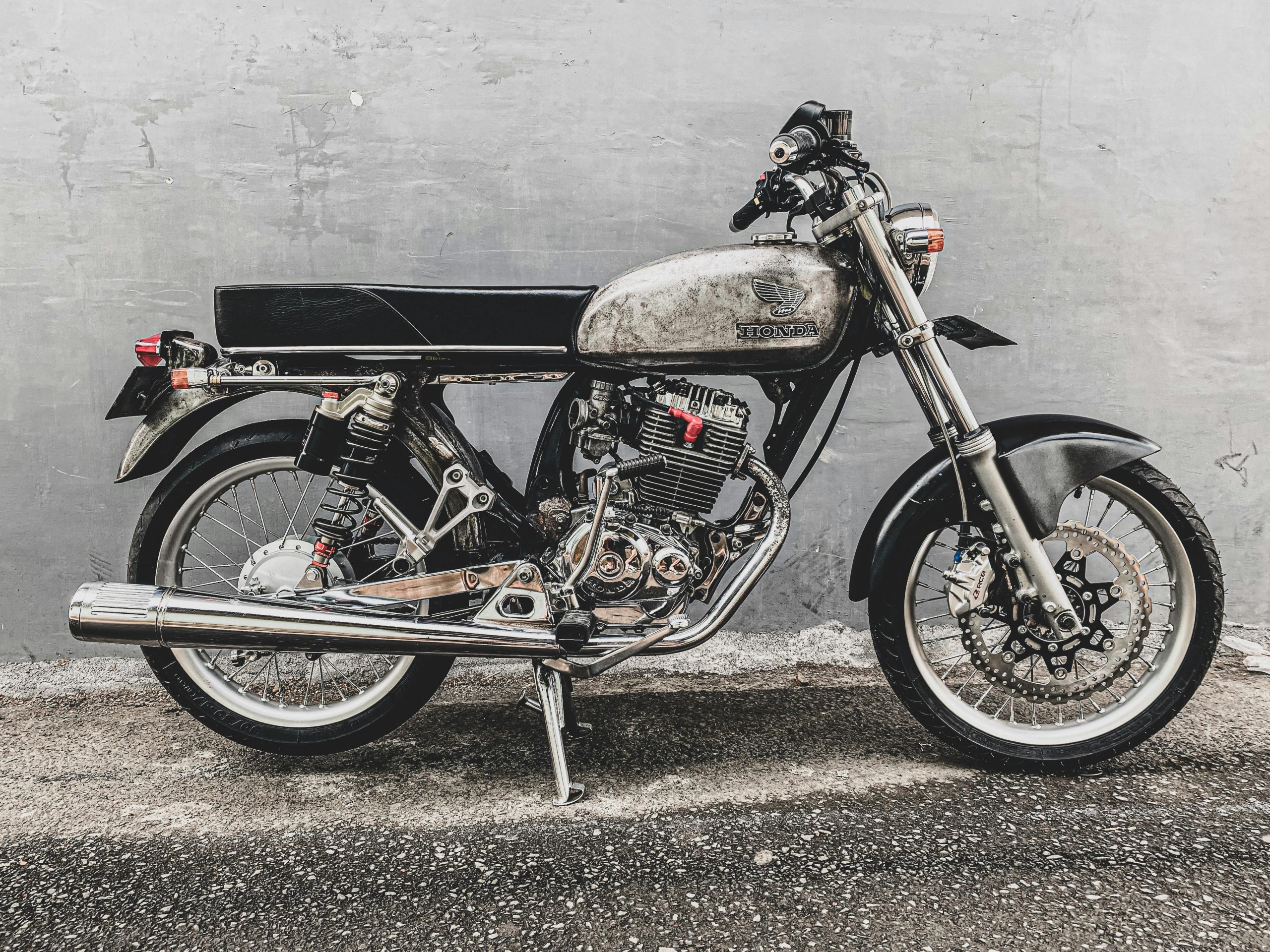 Classic Honda motorcycle parked against a textured gray wall, showcasing chrome details and retro style.